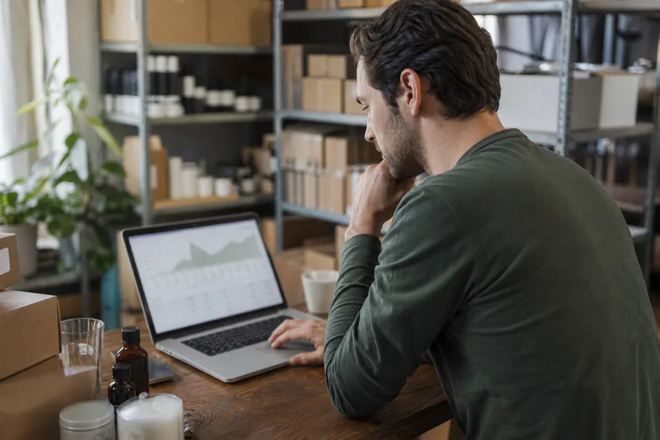 Store owner reviewing a sales chart on a laptop in a small ecommerce studio