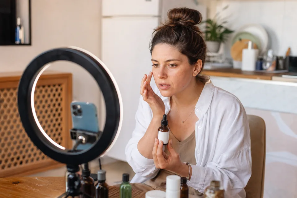 Adult creator filming a skincare product review with a phone on a tripod in a bright kitchen