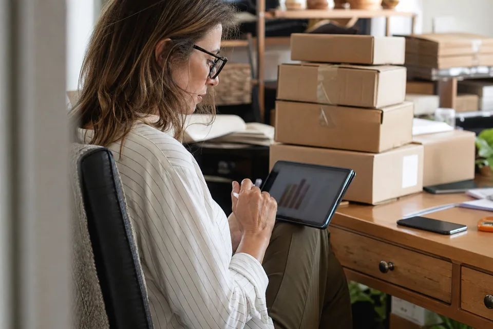 Store owner checking orders on a tablet beside shipped parcels