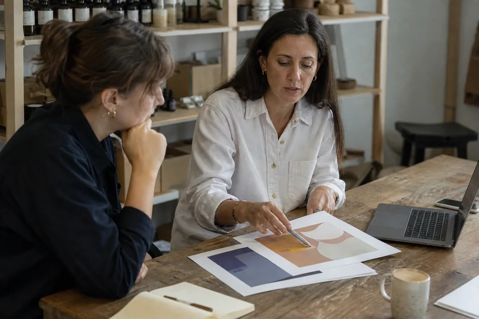 Two people comparing proposals and a spreadsheet at a wooden table